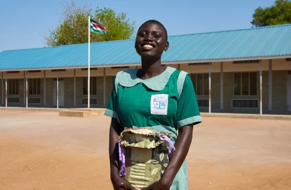 A female student is smiling while holding a school kit received from MCC.